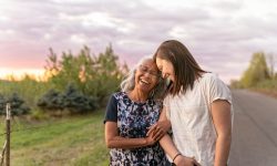 A beautiful senior mom of pacific island descent is walking outdoors with her adult thirty something year old daughter. They are enjoying each others company and soaking in the gorgeous, colorful, sunset.