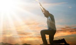 Side View Of A Man Kneeling And Praying Against Cloudy Sky At Sunset