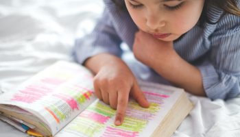 Little girl reading from Bible while lying in bed. Fetita citind din biblie in timp ce sta intinsa in pat.