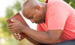 Mature African American man praying and reading the Bible.