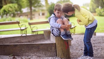 Girl Supporting Sad Boy Sitting Alone on Playground