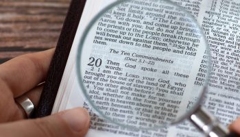 Human hand holding a magnifying glass over open holy bible book of Exodus verses for Ten Commandments. Top view. A close-up. Studying God's righteous spiritual Law, biblical concept.